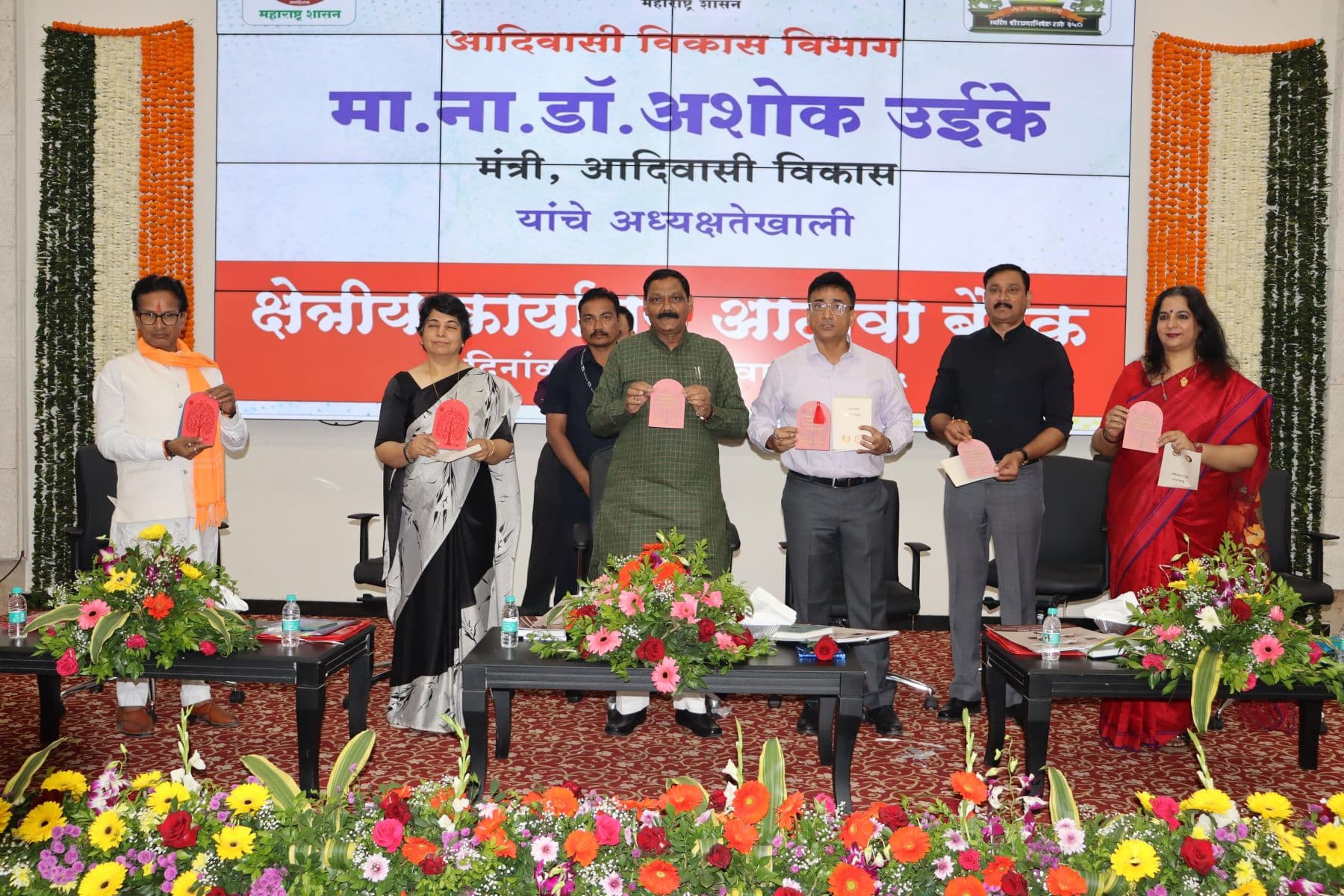 आदिवासी विकास मंत्री मा.ना.डॉ. अशोक उईके यांच्या अध्यक्षतेखालील क्षेत्रीय कार्यालय आढावा बैठकीत व्यासपीठावर सात मान्यवर प्रकाशन करताना; मागील पडद्यावर कार्यक्रमाचे नाव