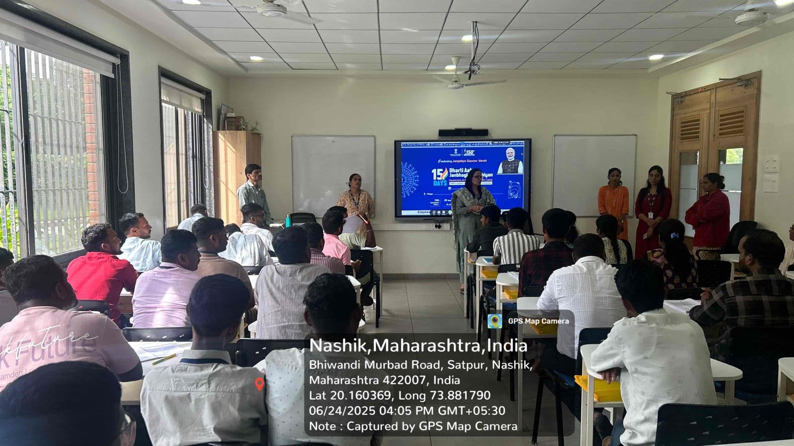 नाशिक येथील प्रशिक्षण कक्षात सुमारे तीस सहभागींसमोर उभ्या राहून मार्गदर्शन करणाऱ्या महिला अधिकारी; पडद्यावर 'धरती आबा जनभागीदारी अभियान' मोहिमेचे सादरीकरण